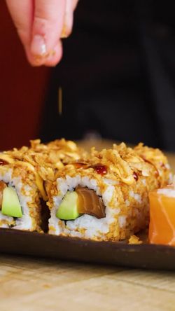 Sushi à emporter garni d'avocat et poisson, préparé dans un restaurant japonais avec finition croustillante et sauce.