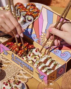 Sushis variés dans une boîte colorée avec des mains utilisant des baguettes pour les prendre, concept de livraison sushi.