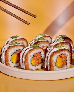 Sushi à emporter présenté sur une assiette, garni d'oignons verts, avec des baguettes au-dessus.