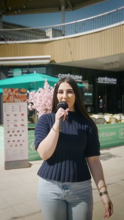 Une jeune femme parle dans un micro devant le restaurant japonais Coté Sushi Tours, avec terrasse et décorations florales.