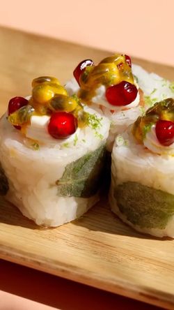 Sushis garnis de fruits de la passion et graines de grenade, présentés sur un plateau en bois au restaurant japonais.