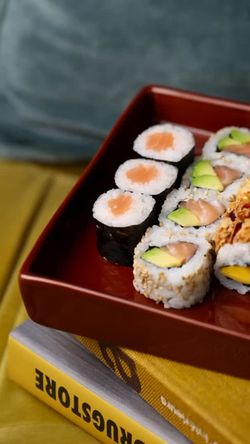 Sushi variés comprenant makis au saumon et rouleaux avec avocat dans un plateau rectangulaire rouge.