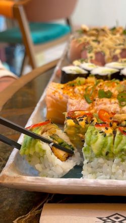 Sushi à emporter avec assortiment varié présenté sur un plateau, incluant makis et boissons en arrière-plan.