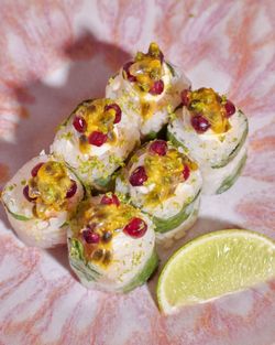 Sushi à emporter présenté avec des graines de grenade et une tranche de citron vert au côté dans une assiette colorée.
