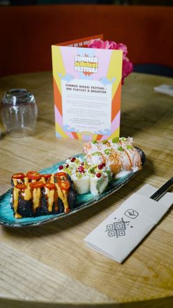 Assortiment de sushis sur un plateau vert avec menu coloré et cure-dents sur une table en bois dans un restaurant japonais.