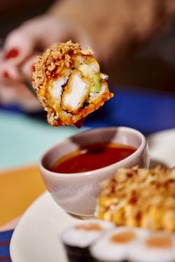 Sushi croustillant avec garniture de poulet et avocat, trempé dans une sauce soja rouge dans un bol en céramique.