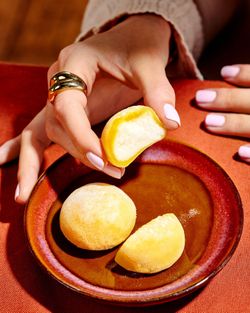 Mains tenant un mochi jaune, posé sur une assiette en terre cuite avec deux autres mochis jaunes.