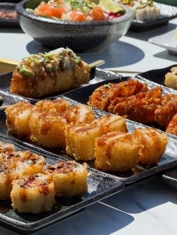 Différents types de sushis croustillants et sauce Teriyaki présentés sur des assiettes noires sur une table claire.