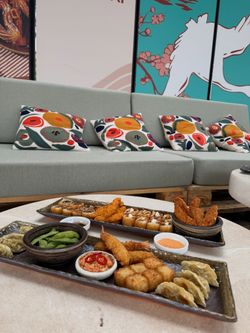 Plateaux variés de cuisine japonaise comprenant sushi, gyoza, crevettes panées et edamame dans un restaurant japonais.