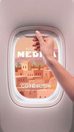 Main tenant la poignée d'une fenêtre d'avion avec illustration de style Méditerranéen et logo Côté Sushi visible