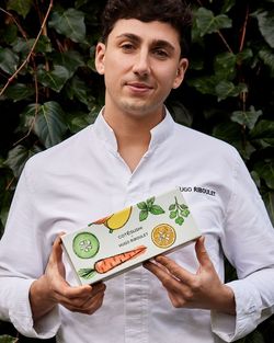 Chef en tenue blanche tenant une boîte de sushi Côté Sushi Brest avec illustrations de légumes colorés