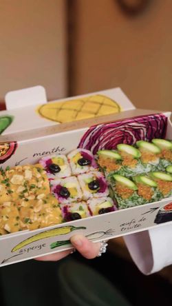 Plateau de sushis à emporter variés avec différentes garnitures, présenté dans une boîte écologique.