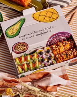 Boîte ouverte contenant des sushis variés, décorée avec des illustrations de fruits et légumes.