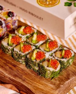 Sushi à emporter avec saumon, avocat et œufs de poisson présentés sur un plateau en bois pour livraison rapide.