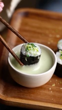 Sushi frais plongé dans une sauce crémeuse, présenté sur un plateau en bois dans un restaurant japonais.