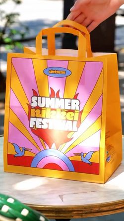 Sac de livraison jaune de Côté Sushi avec inscription Summer Nikkei Festival sur une table en extérieur.