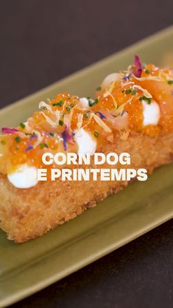 Corn dog garni de perles orange, crème et herbes, présenté sur une assiette rectangulaire verte dans un restaurant japonais.