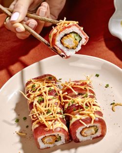 Sushi à emporter avec garniture croustillante et sauce, présenté dans une assiette blanche au restaurant japonais.