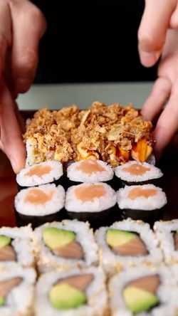 Sushis variés avec avocat, saumon et tempura, présentés sur une assiette tenue par des mains.