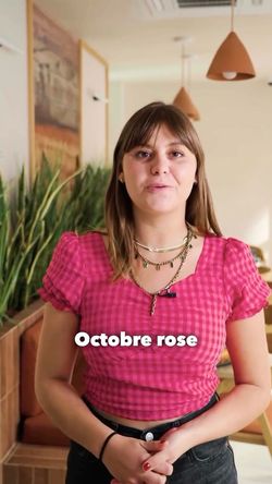Jeune femme en haut rose à carreaux dans un restaurant japonais, avec plantes en arrière-plan, texte "Octobre rose" affiché