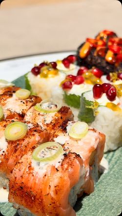 Assortiment de sushis variés avec saumon grillé, garnitures colorées sur un plat vert clair.