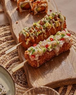 Brochettes de sushi croustillants garnies d'avocat, sauce et piments, présentées sur une planche en bois