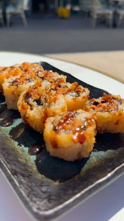 Sushis à emporter présentés sur un plateau noir, garnis de sauce et croustillants, en extérieur au restaurant.