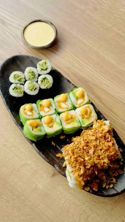 Plateau de sushi à emporter comprenant différents makis et rolls avec une sauce en accompagnement, sur une table en bois
