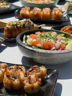 Assortiment de sushi à emporter et plats japonais servis sur plusieurs assiettes noires dans un restaurant japonais.
