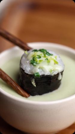 Sushi à emporter garni de sauce crémeuse et d'oignons verts dans un bol de sauce claire avec baguettes en bois.