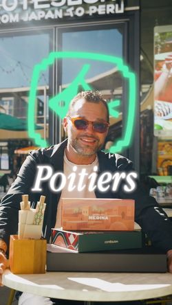 Homme portant des lunettes de soleil assis à une table avec des boîtes de sushis devant un restaurant japonais à Poitiers.
