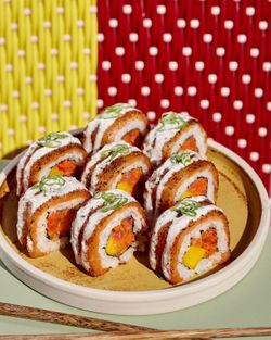 Sushi à emporter sur une assiette, avec une garniture colorée et des touches de sauce, présentés avec des baguettes.