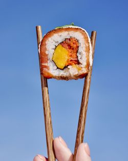 Sushi à emporter tenu par des baguettes en bois sur fond de ciel bleu chez Côté Sushi Aubagne.