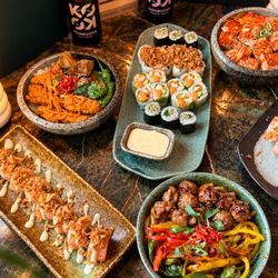 Plateaux variés de sushis, bols de riz et légumes, présentés sur une table en pierre avec boissons kombucha.