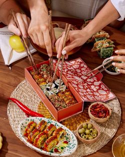 Sushi à emporter servi dans une boîte avec des baguettes, accompagné d'olives, piments, et autres plats japonais.