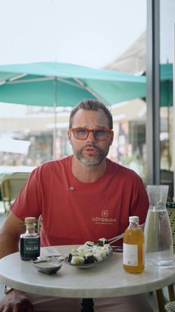 Homme portant un t-shirt Côté Sushi Poitiers dégustant des sushis dans un restaurant avec boissons sur la table.