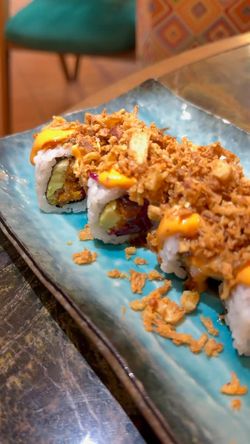Sushi croustillants garnis de sauce et d'oignons frits servis sur une assiette bleue dans un restaurant japonais.