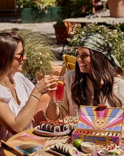 Deux femmes trinquent avec des boissons près d'un plateau de sushi à emporter dans un restaurant japonais.