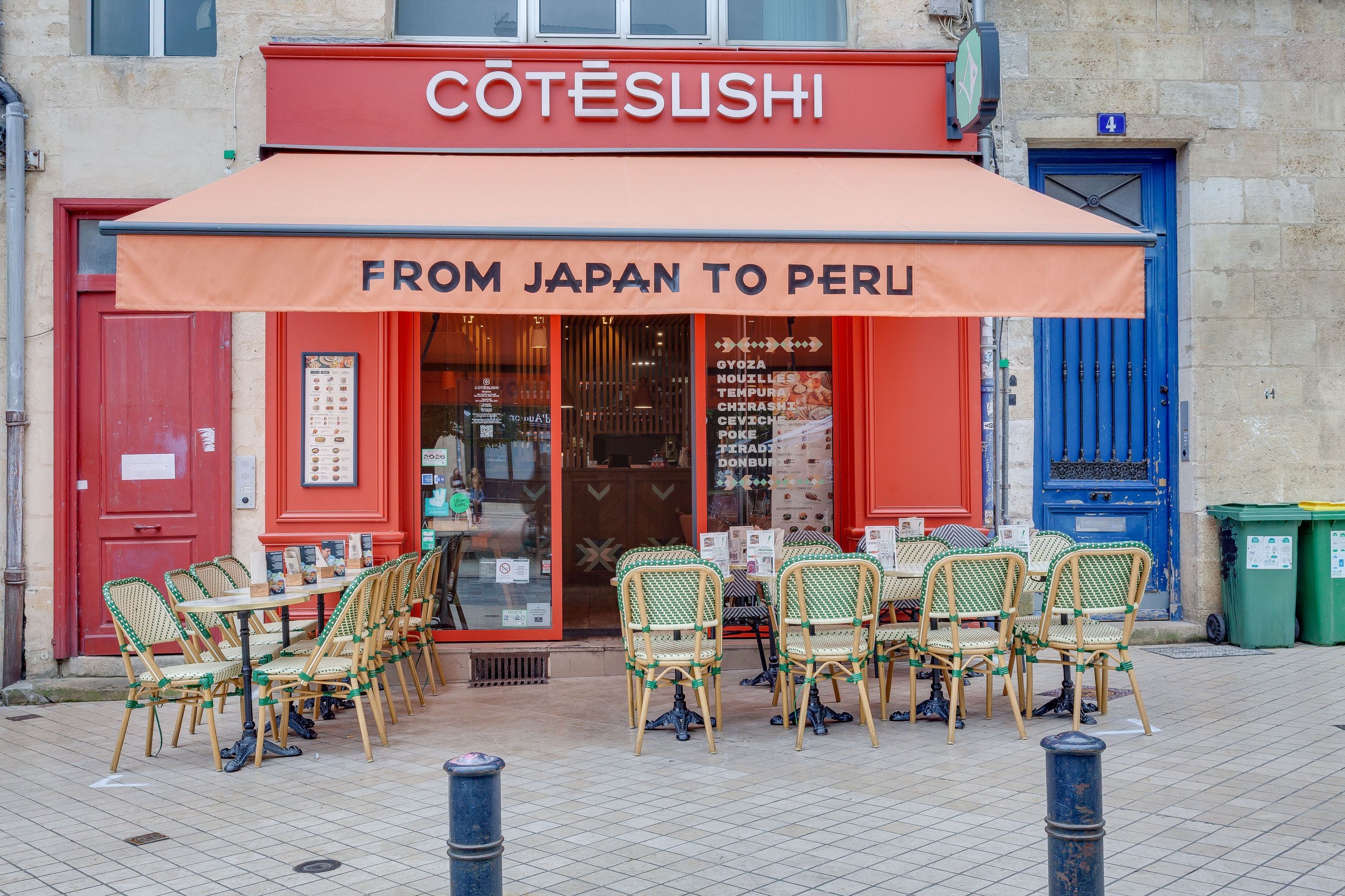 Façade rouge de Côté Sushi Bordeaux avec terrasse extérieure et chaises vertes sur trottoir piéton