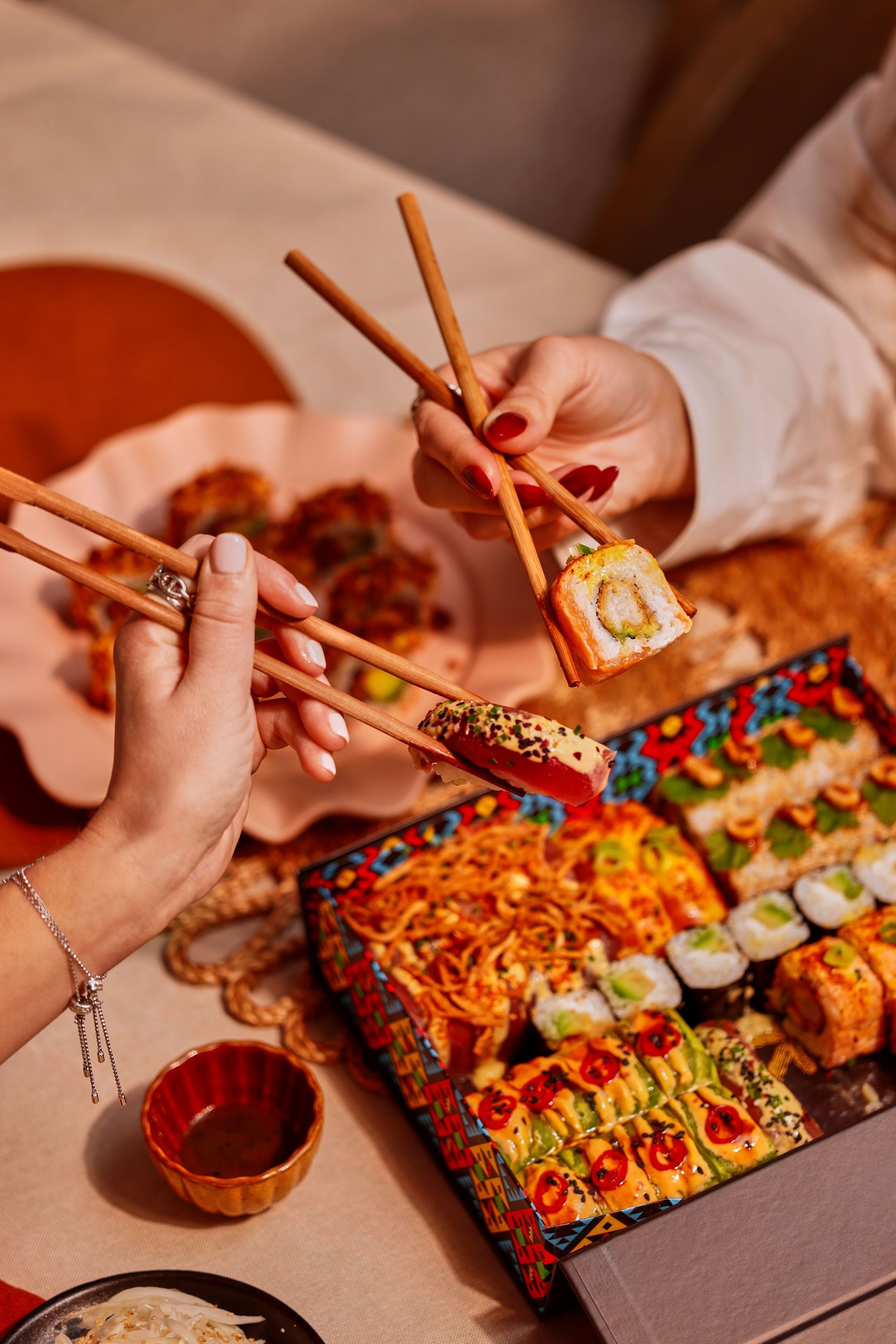 Sushi variés en plateau coloré avec mains utilisant des baguettes pour saisir des morceaux dans un restaurant japonais