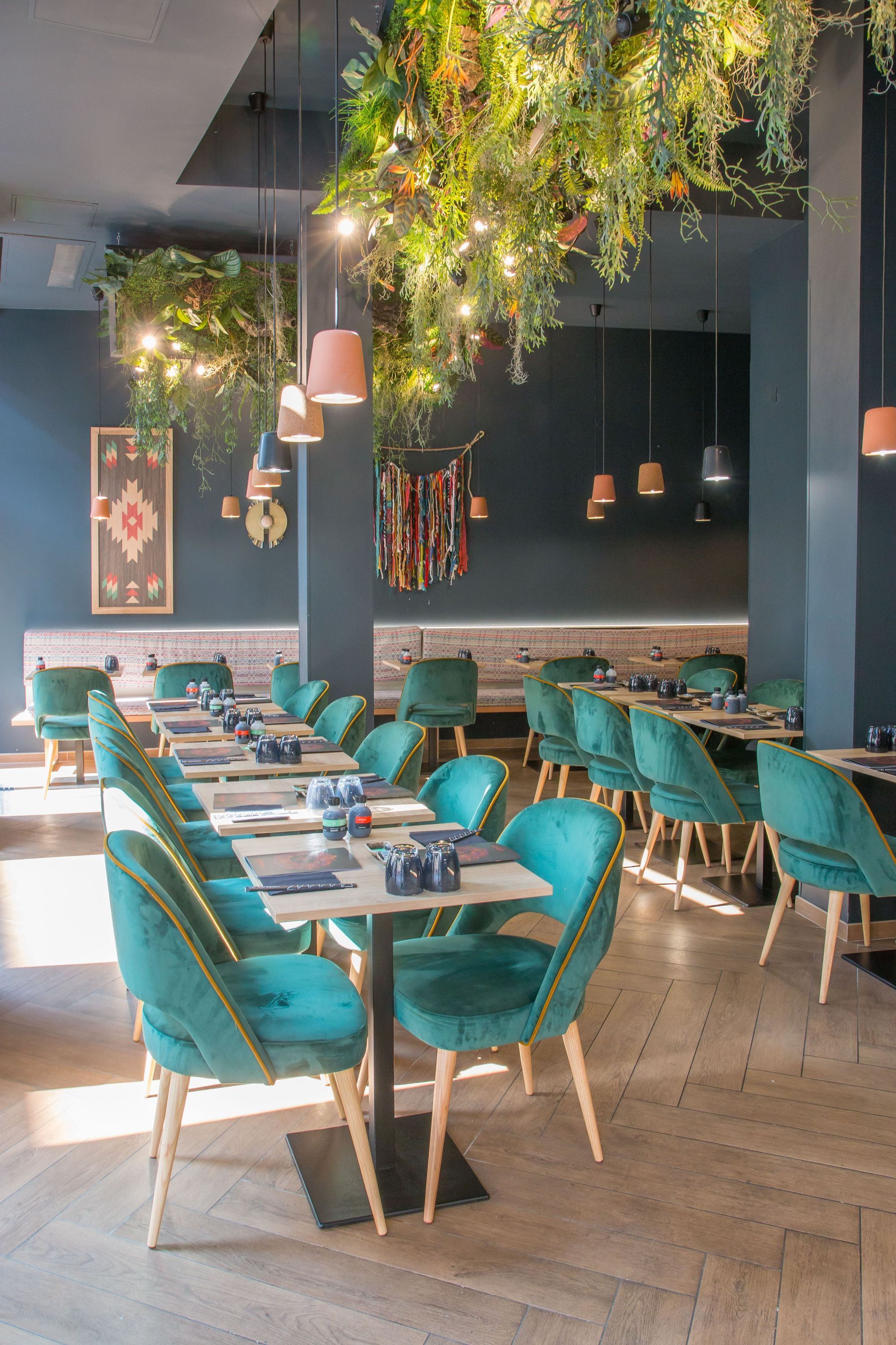 Restaurant japonais avec décoration végétale suspendue et chaises vertes élégantes autour des tables en bois clair.