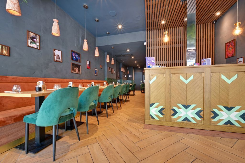 Intérieur moderne d'un restaurant japonais avec chaises vertes, banquettes en cuir orange et éclairage suspendu.