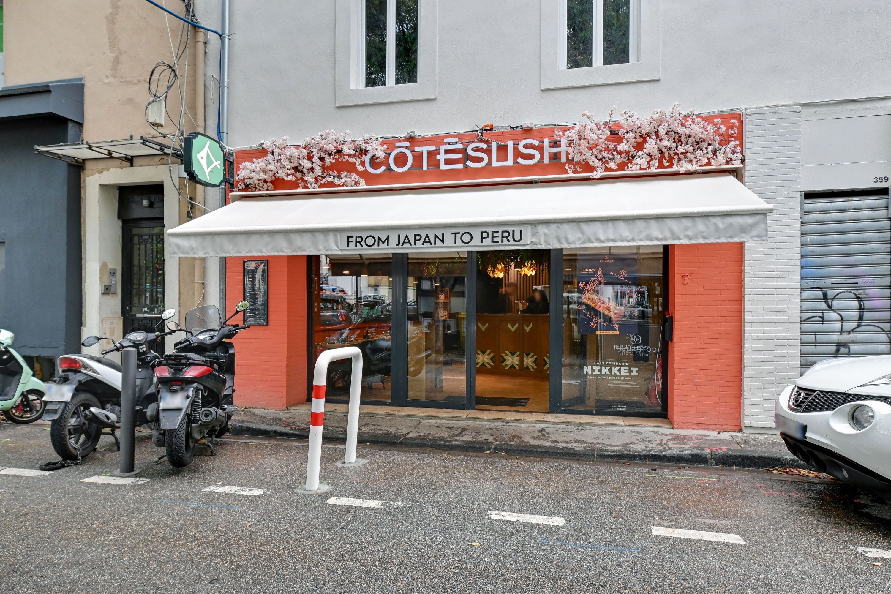 Façade moderne d'un restaurant japonais avec enseigne Côté Sushi et décoration florale extérieure.