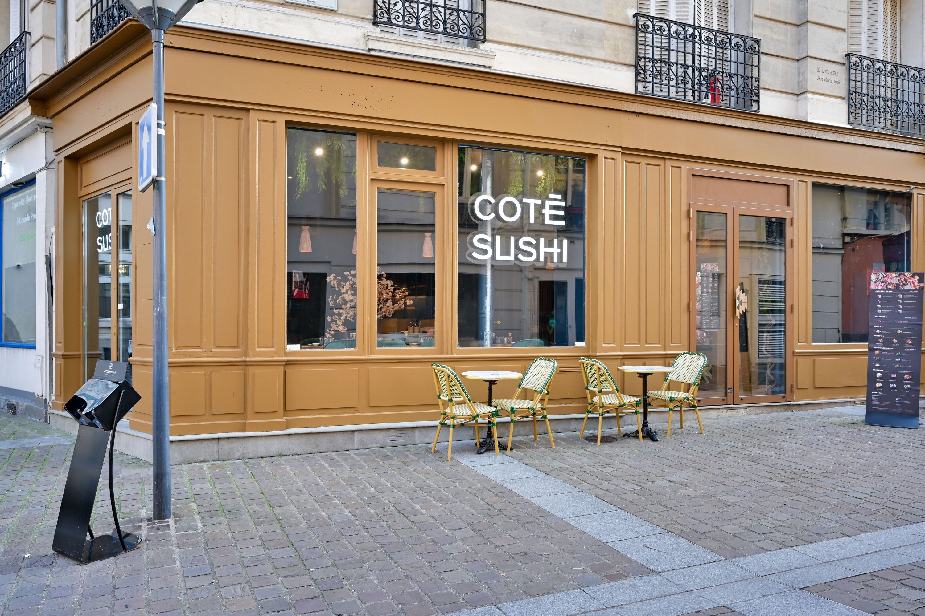 Façade marron clair du restaurant japonais Côté Sushi avec tables et chaises en terrasse sur une rue pavée.