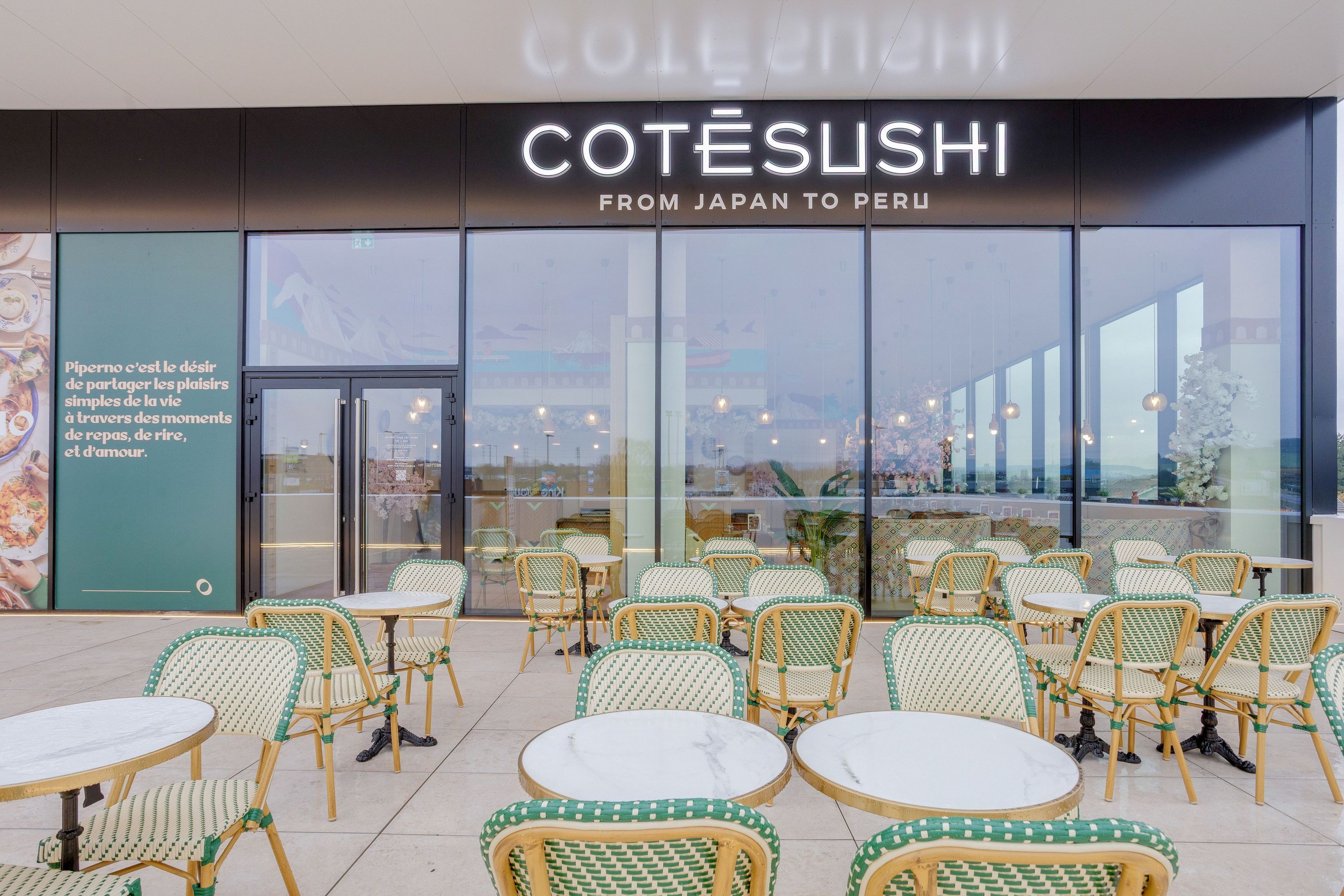 Terrasse avec tables rondes et chaises en osier vert et blanc devant le restaurant japonais Côté Sushi à Reims Cormontreuil.