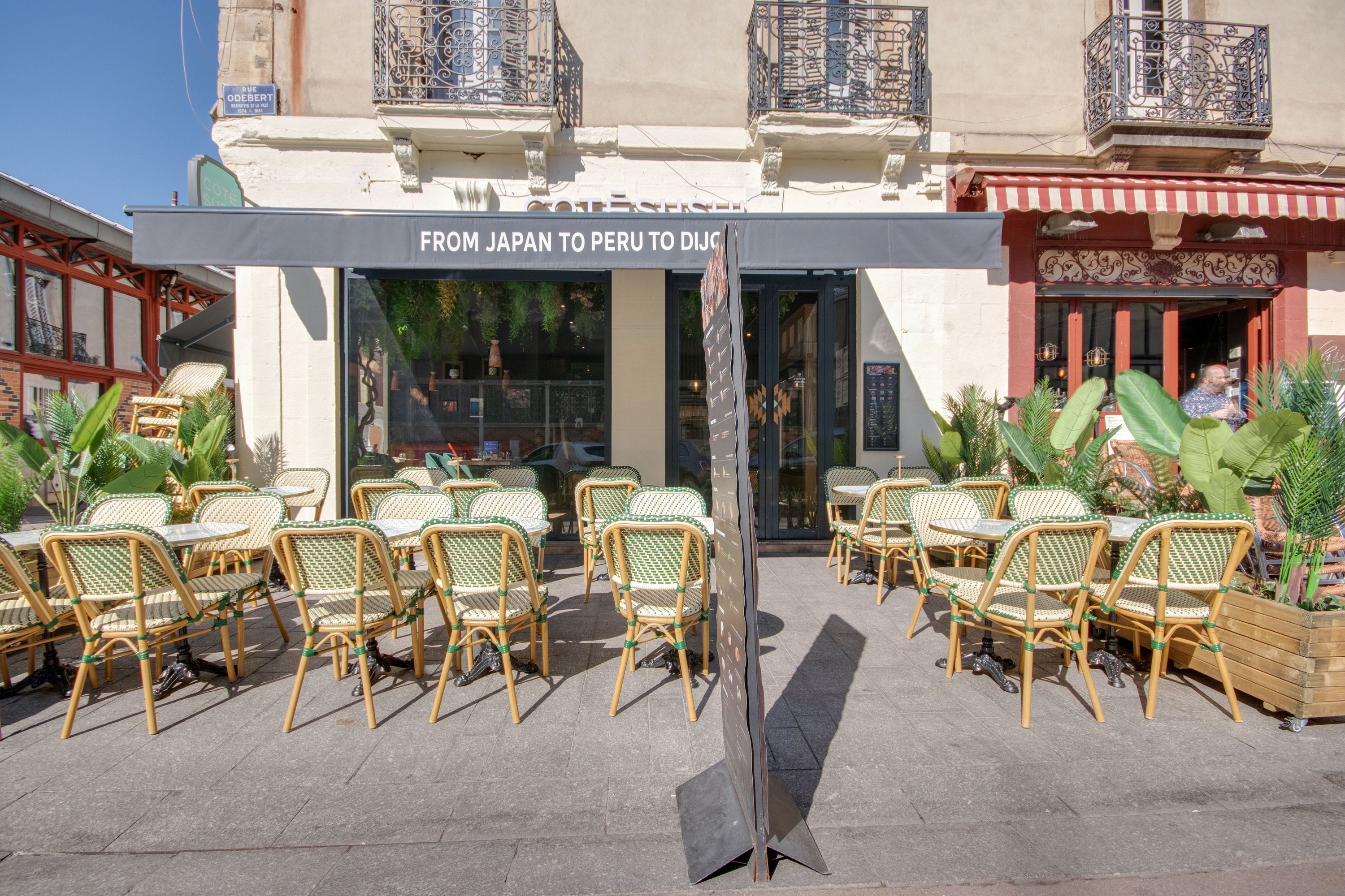 Terrasse extérieure d'un restaurant japonais à emporter avec tables et chaises en osier sous un store gris