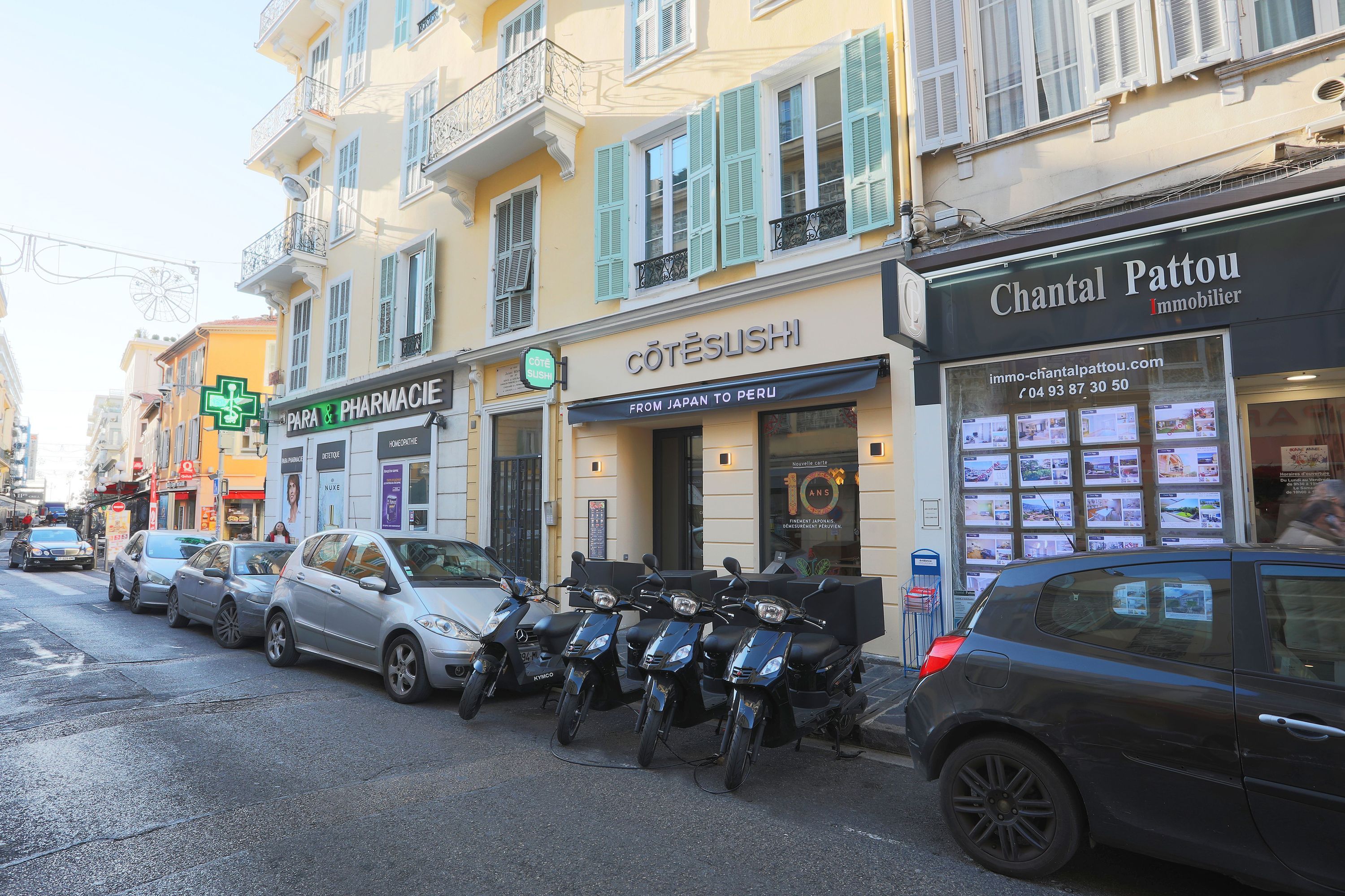 Façade du restaurant japonais Côté Sushi Nice Macarani avec scooters de livraison garés devant sur une rue urbaine.