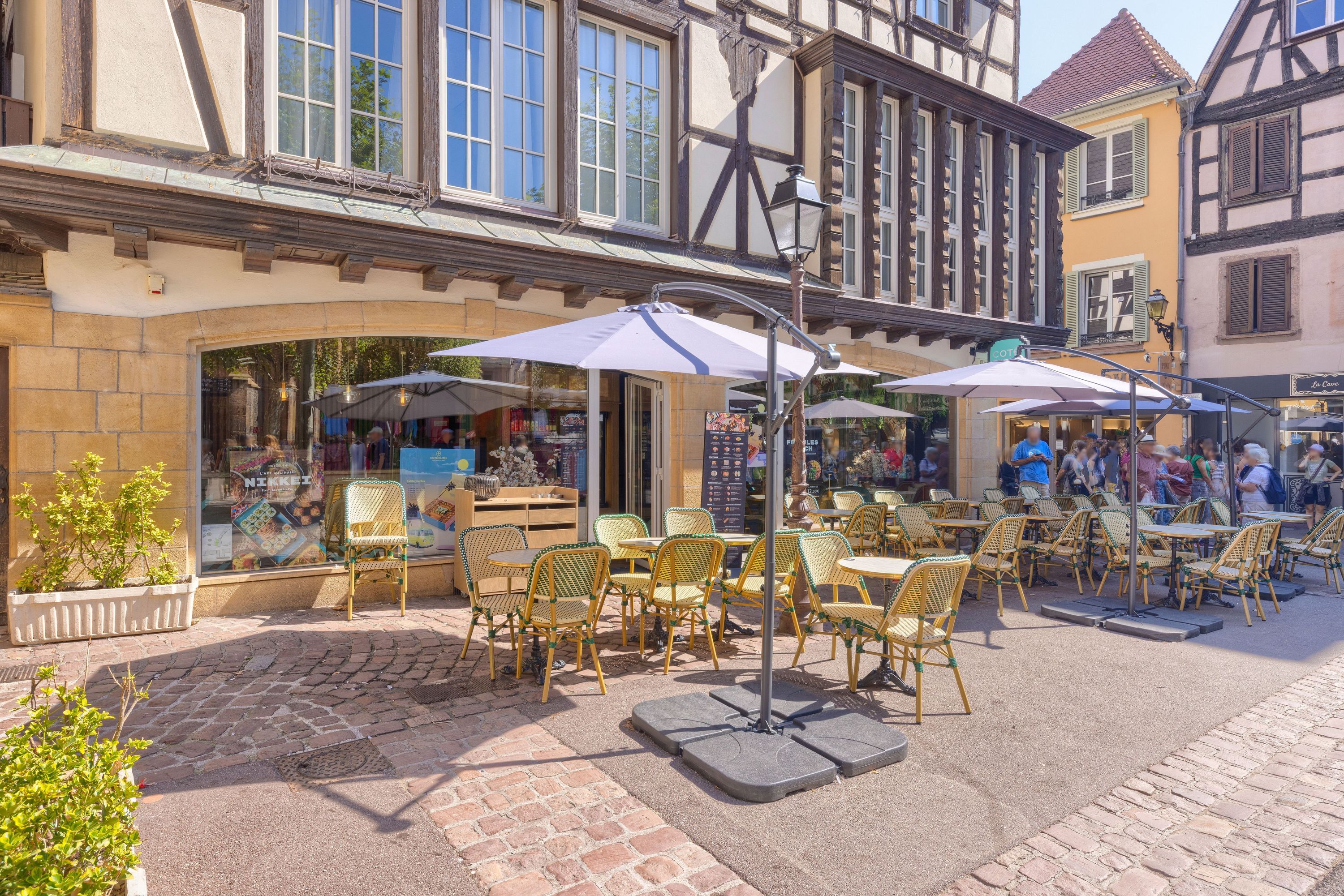Terrasse extérieure avec tables et chaises sous des parasols devant un restaurant japonais en centre-ville de Colmar.