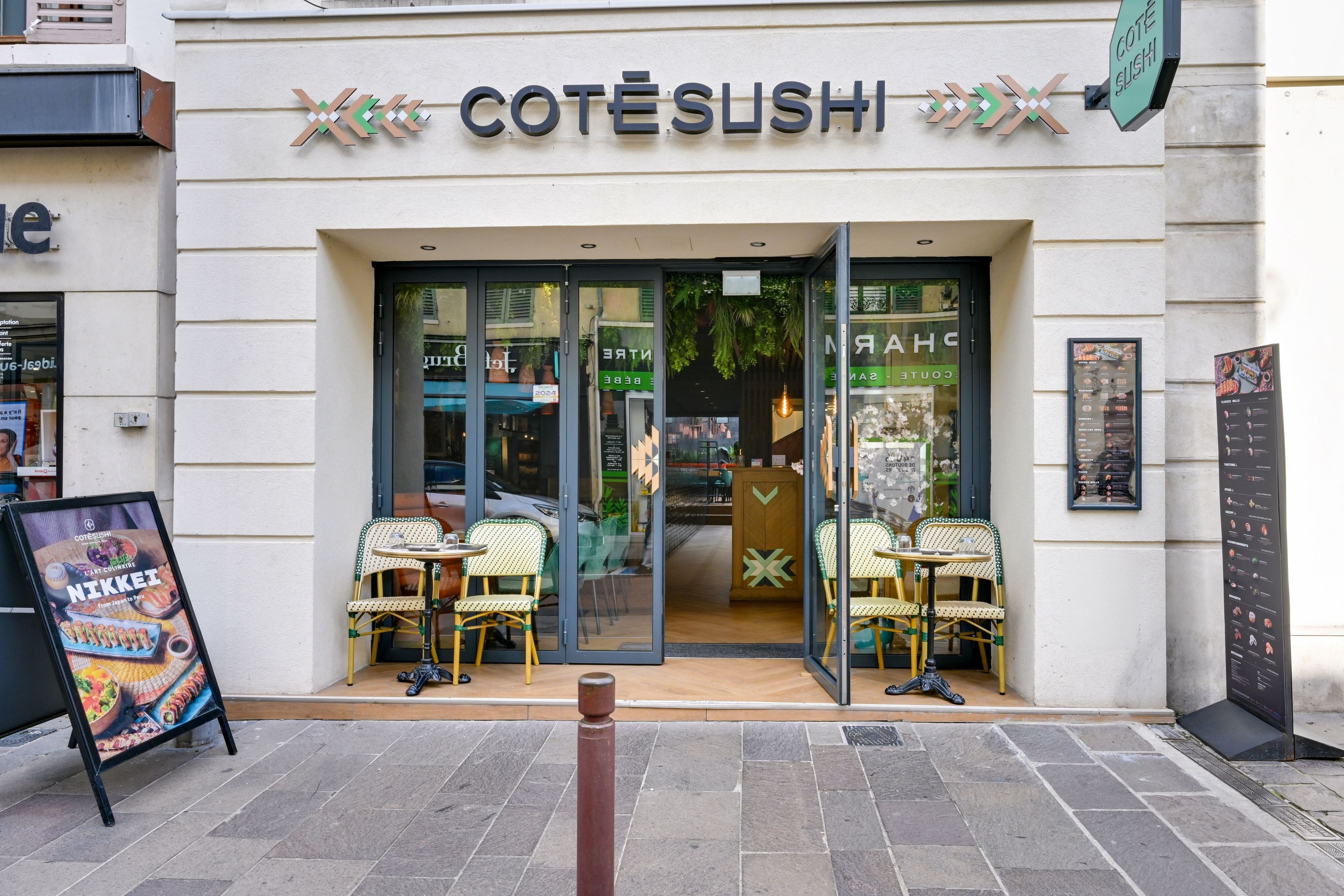 Entrée du restaurant japonais Côté Sushi à Poissy avec deux petites tables et chaises en terrasse, portes vitrées ouvertes.