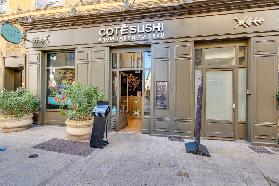 Façade du restaurant Côté Sushi Chelles avec une entrée ouverte et deux grandes plantes en pot sur le trottoir.